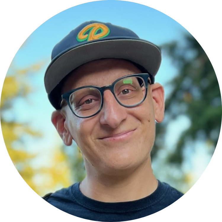 Picture of Drew Tocco. Drew wears a black hat, a black shirt, and dark blue glasses.