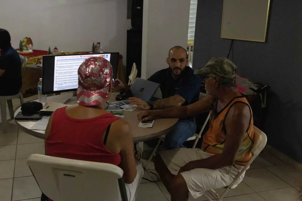 Three people sit around a table and read a slideshow from a desktop computer screen.