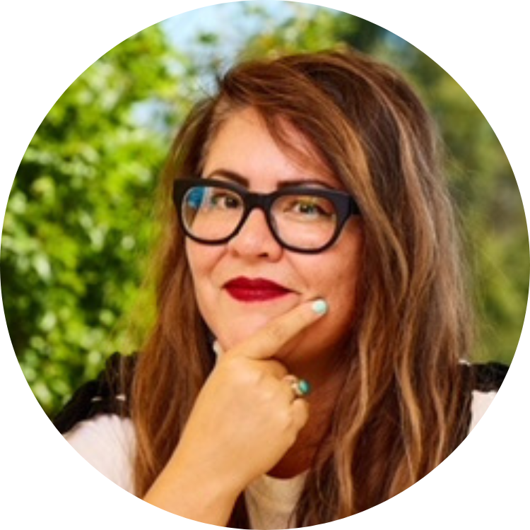 Picture of Jackie Schultz. Jackie stands in front of a nature background wearing a black and white outfit and black glasses.