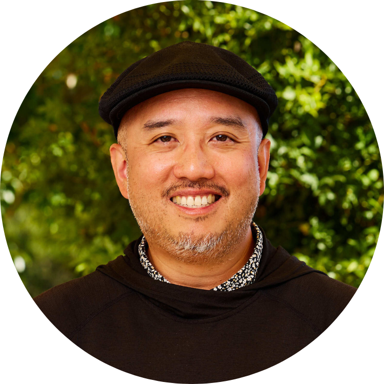 Picture of Joaquin Uy. Joaquin stands in front of a nature background and wears a black top and a black hat.